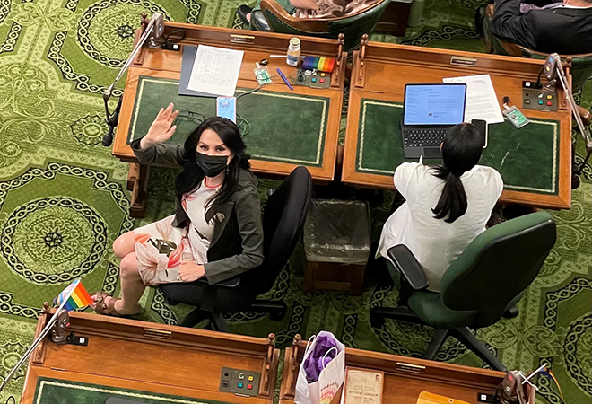 Assemblywoman Rubio sitting in her chair on the Assembly floor looking up and waving