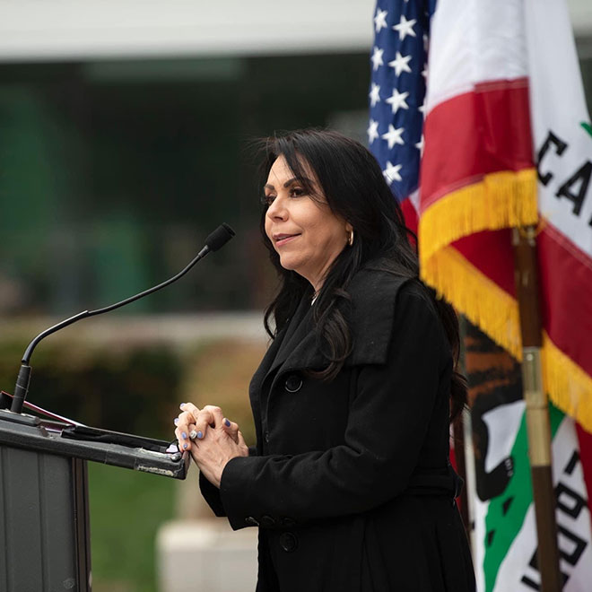 Assemblywoman Blanca Rubio standing at a podium speaking with the CA state flag hanging in the background